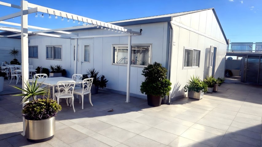Vista exterior del edificio de eventos con pérgola iluminada y terraza