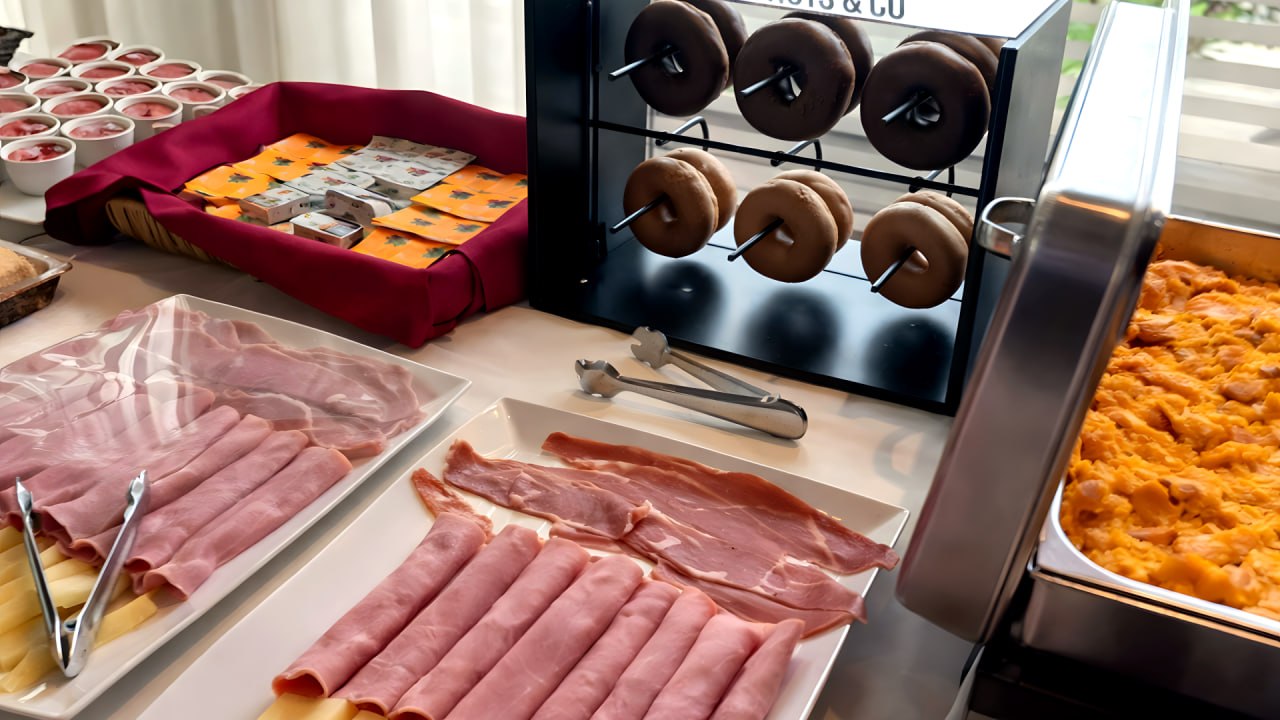 Vista panorámica completa del desayuno buffet con zona caliente, pan y fiambres