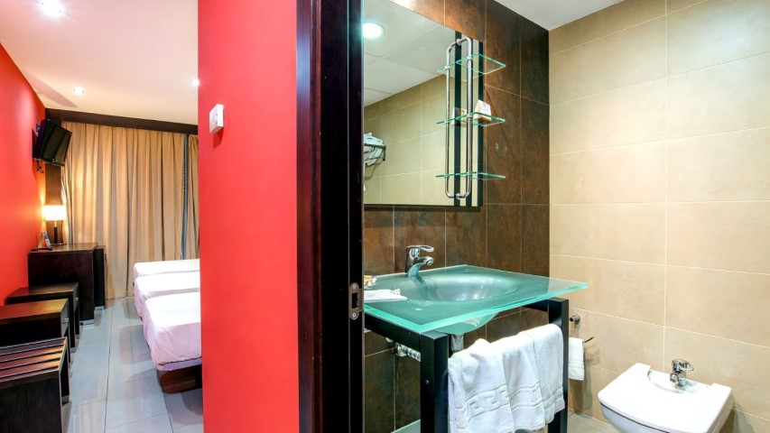 Baño con lavabo de cristal verde y vista a la habitación
